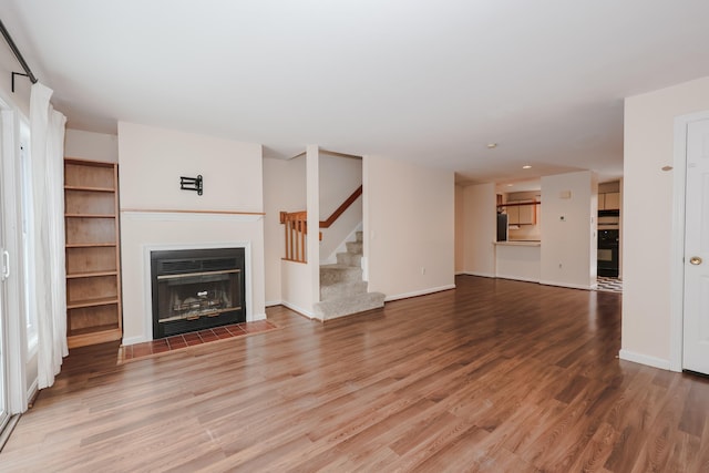 unfurnished living room featuring a fireplace with flush hearth, stairway, baseboards, and wood finished floors