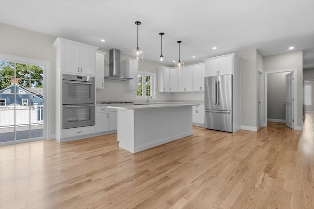 kitchen featuring wall chimney exhaust hood, a center island, stainless steel appliances, light countertops, and pendant lighting