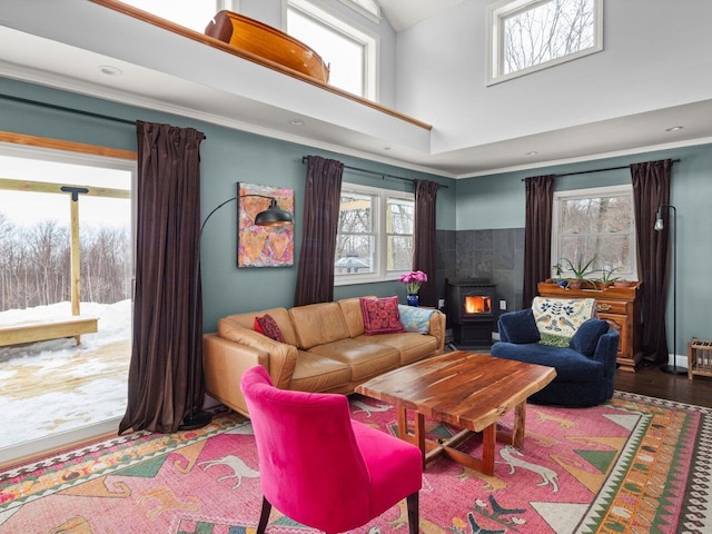 living room featuring a towering ceiling, wood finished floors, a wood stove, and crown molding