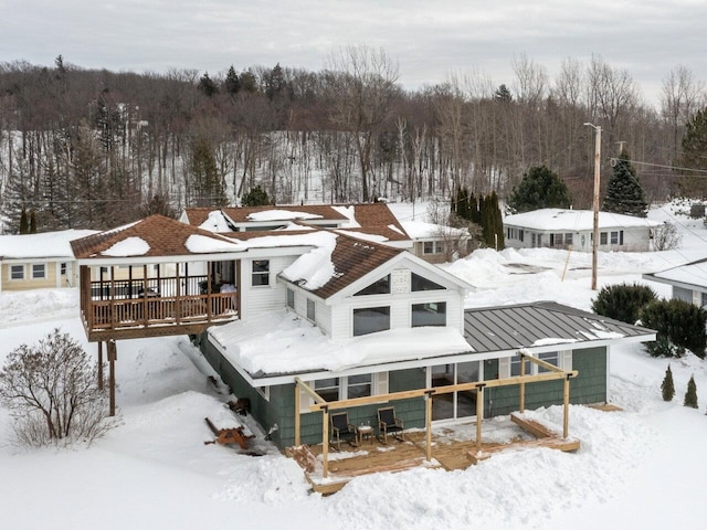 snow covered house with a standing seam roof, metal roof, a deck, and a view of trees