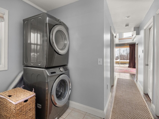 clothes washing area with stacked washer / dryer, tile patterned flooring, and baseboards