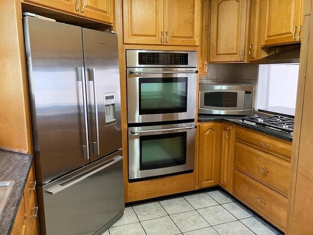 kitchen featuring appliances with stainless steel finishes, brown cabinetry, and dark countertops