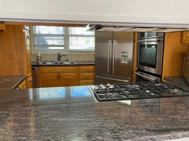 kitchen with dark stone counters, stainless steel appliances, brown cabinetry, and a sink