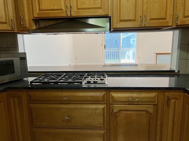 kitchen featuring wall chimney exhaust hood, brown cabinetry, dark countertops, and stainless steel appliances