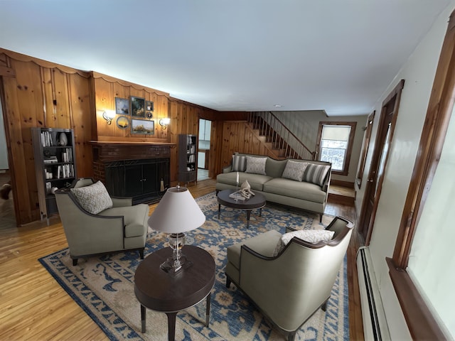 living area with wooden walls, light wood-style flooring, stairway, a brick fireplace, and a baseboard heating unit