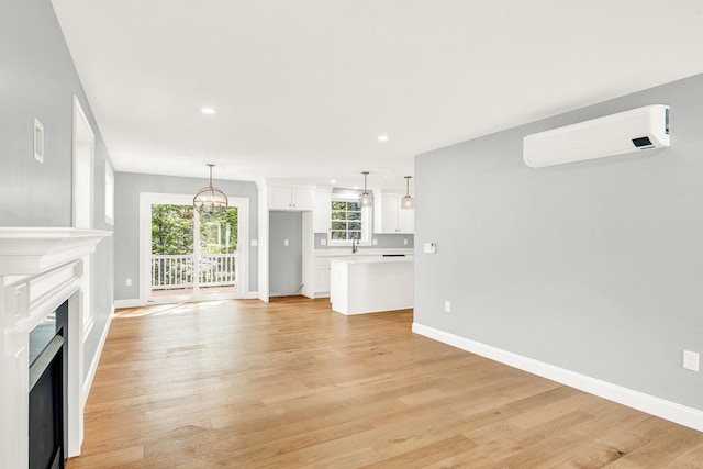 unfurnished living room featuring a fireplace, recessed lighting, light wood-style flooring, an AC wall unit, and baseboards