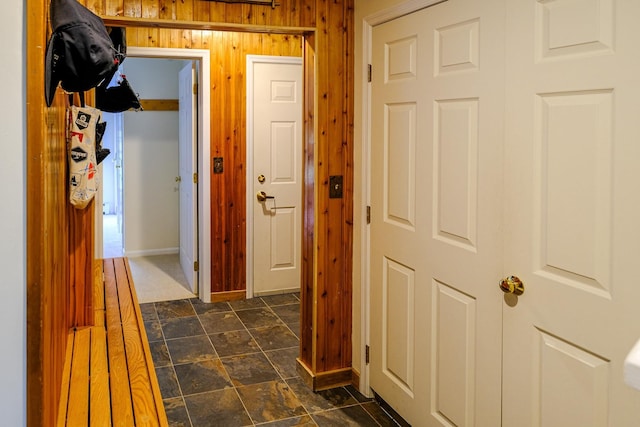 corridor featuring baseboards, stone finish flooring, and wooden walls