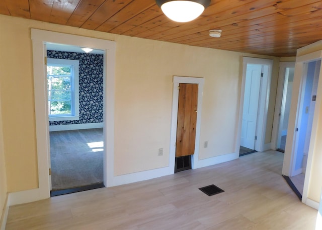 empty room with light wood-type flooring, wooden ceiling, visible vents, and baseboards