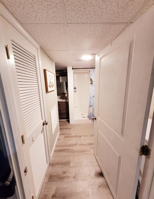 corridor featuring light wood finished floors and a paneled ceiling