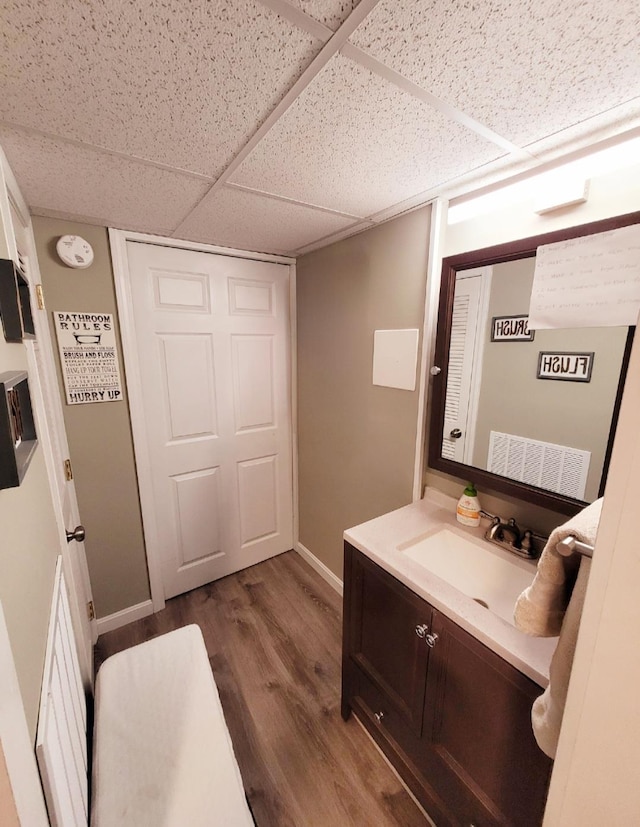 bathroom with a drop ceiling, vanity, baseboards, and wood finished floors