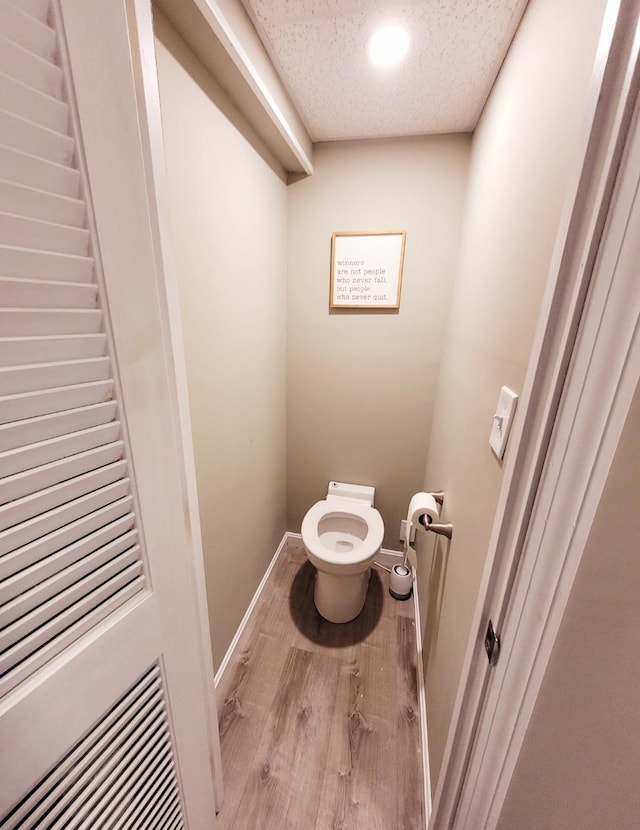 bathroom with baseboards, toilet, wood finished floors, and a textured ceiling