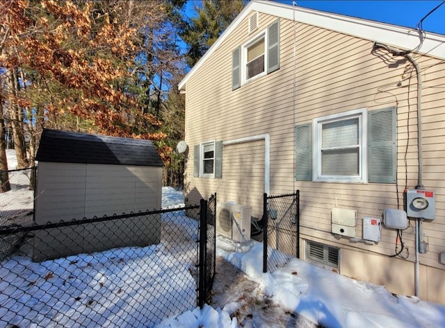 snow covered property with ac unit, a storage unit, an outdoor structure, and fence