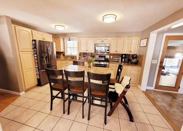 kitchen with decorative backsplash, appliances with stainless steel finishes, a kitchen breakfast bar, cream cabinetry, and a sink