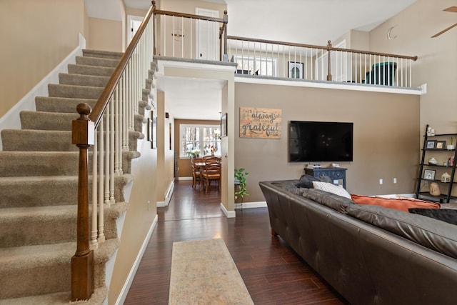 living area with dark wood-style floors, stairway, a towering ceiling, and baseboards