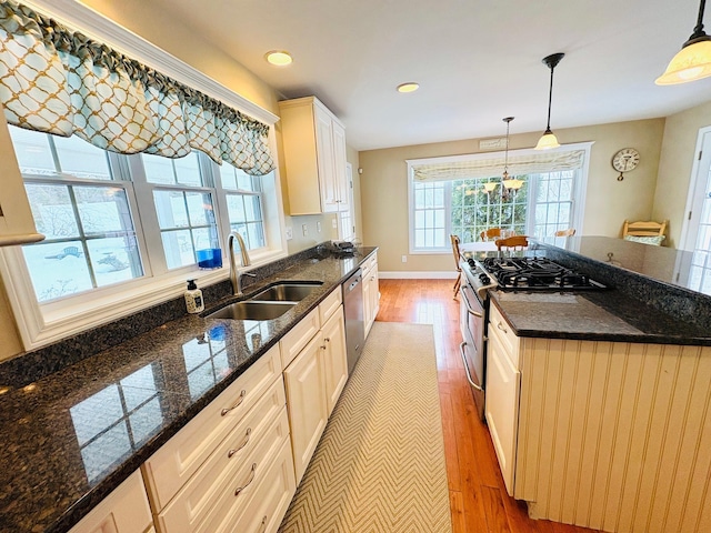 kitchen featuring light wood-style floors, stainless steel appliances, a sink, and decorative light fixtures