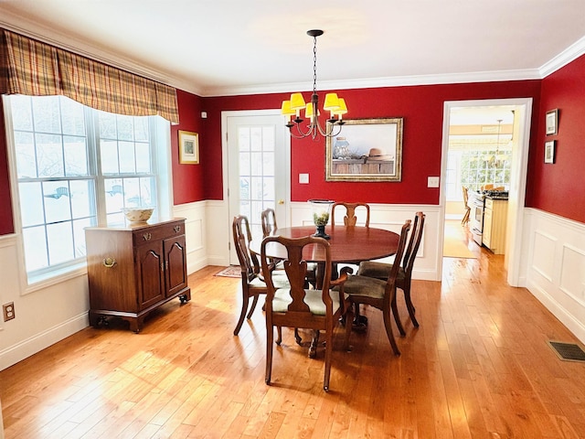 dining room featuring a notable chandelier, visible vents, ornamental molding, wainscoting, and light wood-type flooring