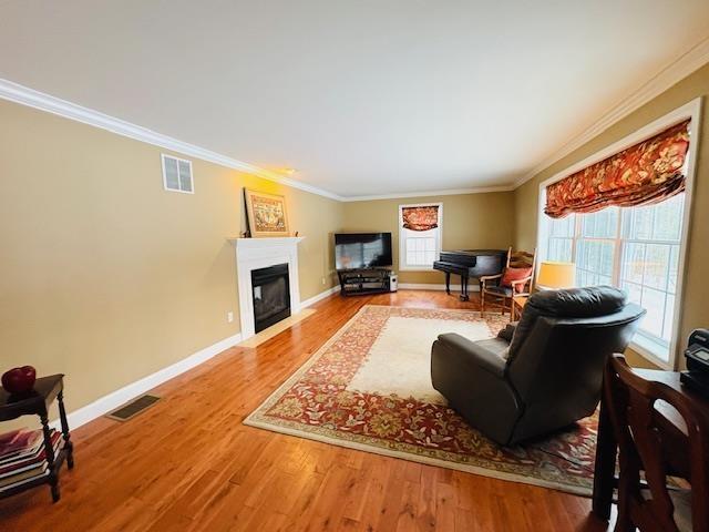 living area with a fireplace with flush hearth, visible vents, a wealth of natural light, and wood finished floors