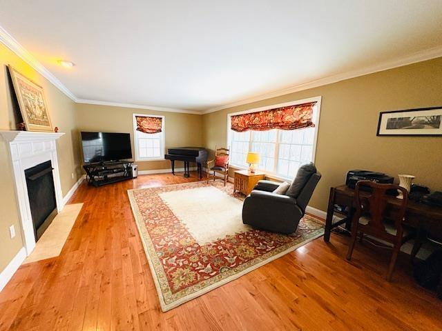 living area featuring ornamental molding, light wood finished floors, a fireplace with flush hearth, and baseboards