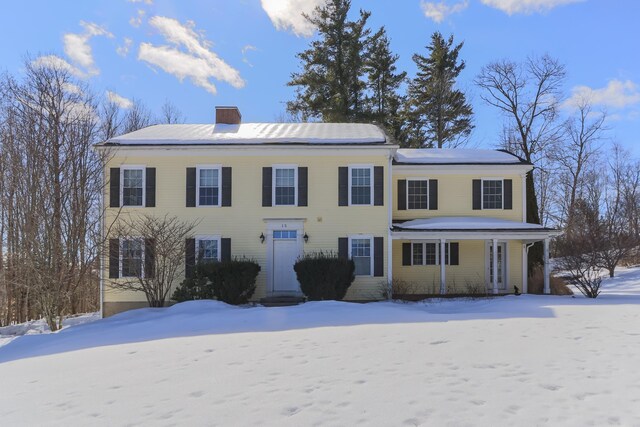 colonial inspired home featuring a chimney, a porch, and roof mounted solar panels