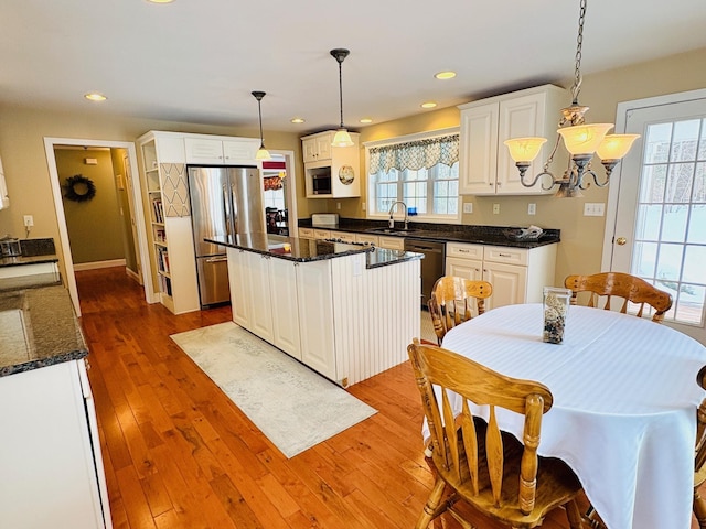 kitchen with a sink, a healthy amount of sunlight, white cabinets, appliances with stainless steel finishes, and hardwood / wood-style floors