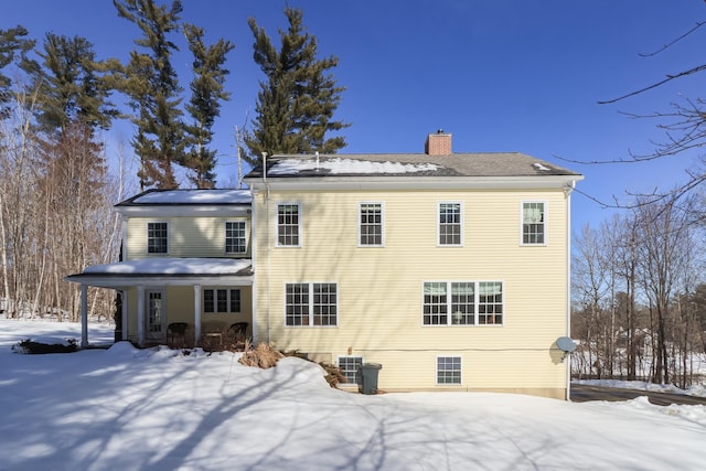 snow covered rear of property with central AC and a chimney