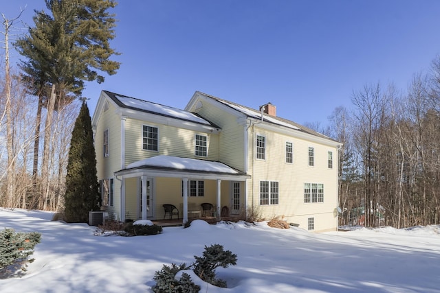 view of front of house with covered porch, a chimney, and central AC unit