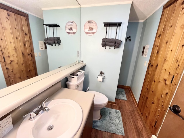 bathroom featuring toilet, ornamental molding, wood finished floors, a textured ceiling, and vanity