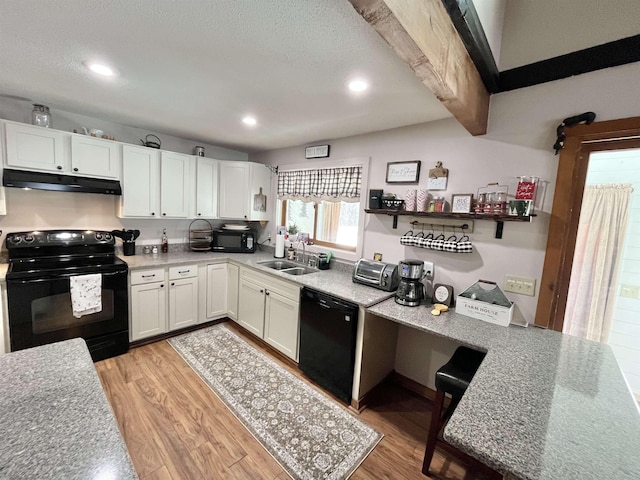 kitchen with under cabinet range hood, a sink, white cabinetry, light wood-type flooring, and black appliances