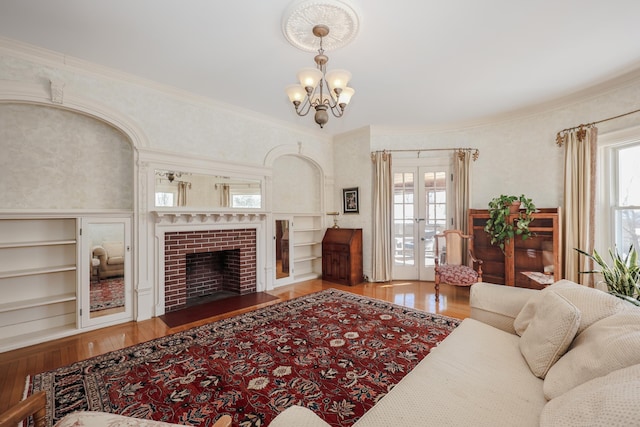 living area with french doors, a notable chandelier, ornamental molding, a brick fireplace, and wood finished floors