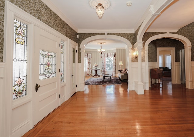 foyer featuring wallpapered walls, light wood-style flooring, arched walkways, and wainscoting