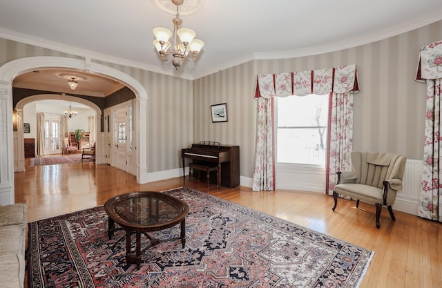 living area with wallpapered walls, arched walkways, a notable chandelier, and hardwood / wood-style floors