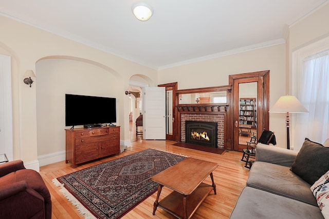 living room featuring light wood-style floors, a brick fireplace, crown molding, and baseboards