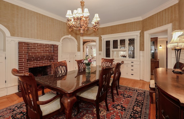 dining area featuring arched walkways, light wood-style flooring, wallpapered walls, an inviting chandelier, and crown molding