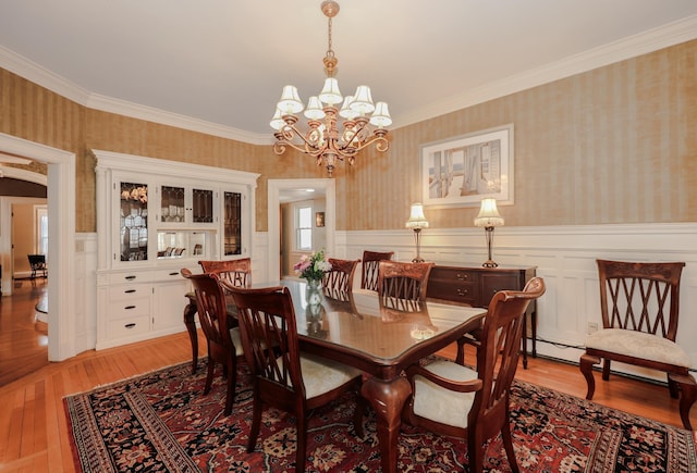 dining room featuring light wood-style floors, a wainscoted wall, crown molding, and wallpapered walls