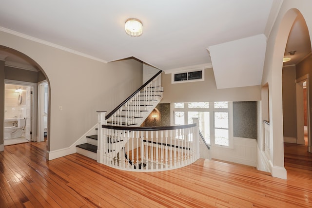 stairs featuring arched walkways, baseboards, a wainscoted wall, hardwood / wood-style floors, and crown molding