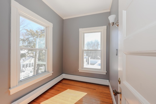 interior space with baseboards, baseboard heating, crown molding, and wood finished floors