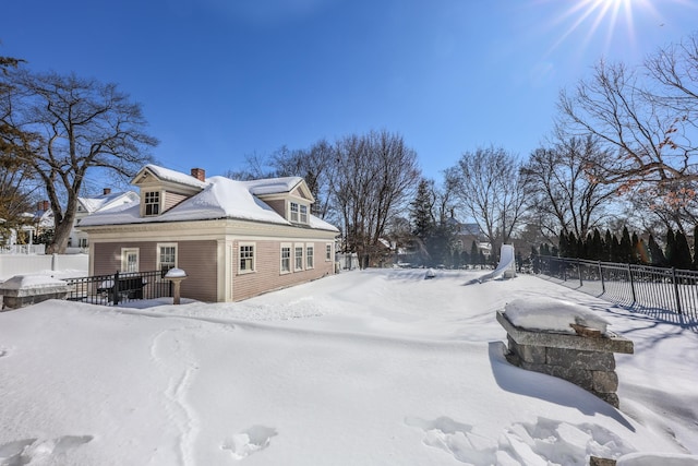 view of snowy exterior with a chimney and fence