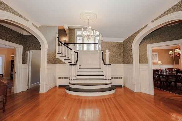 stairs featuring radiator, wallpapered walls, and a notable chandelier