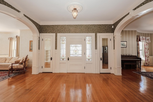 foyer entrance with arched walkways, ornamental molding, plenty of natural light, and hardwood / wood-style flooring