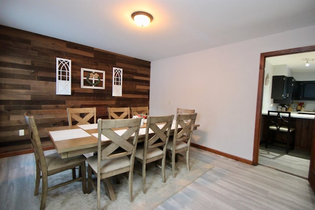 dining room featuring baseboards, light wood-style flooring, and wooden walls