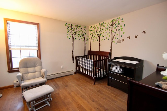 bedroom featuring a baseboard radiator, baseboards, baseboard heating, a nursery area, and wood-type flooring