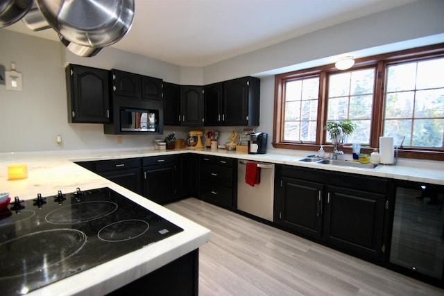 kitchen with dishwasher, dark cabinets, black electric cooktop, light countertops, and a sink