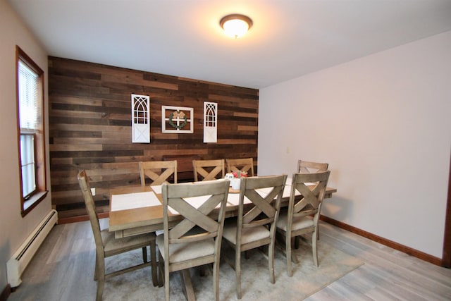 dining room with a baseboard radiator, an accent wall, wood walls, wood finished floors, and baseboards