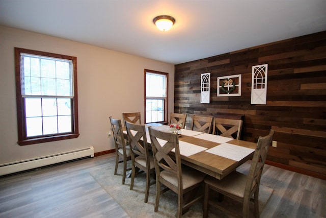 dining room with wood walls, baseboards, baseboard heating, and wood finished floors