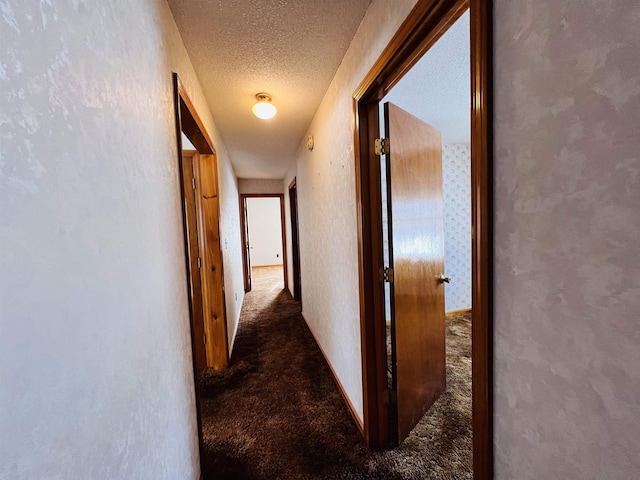 hallway with carpet floors, a textured wall, a textured ceiling, and baseboards