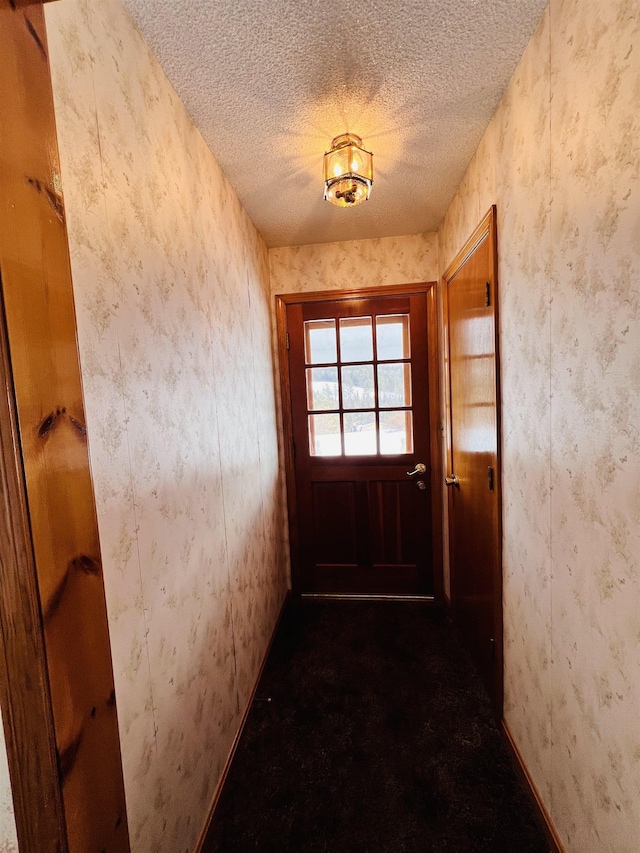 doorway to outside with wallpapered walls and a textured ceiling