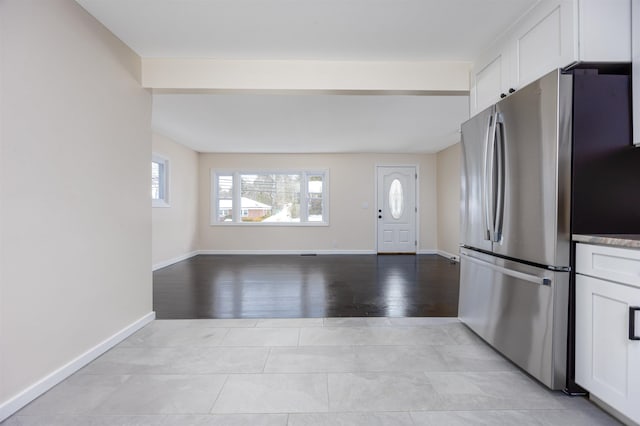 kitchen featuring open floor plan, baseboards, freestanding refrigerator, and white cabinets