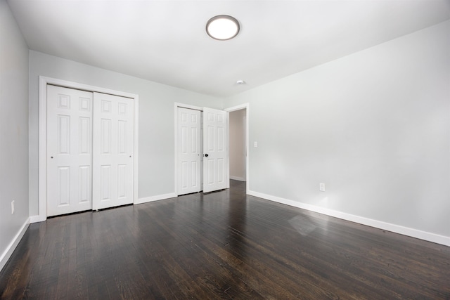 unfurnished bedroom featuring dark wood-style flooring, baseboards, and two closets