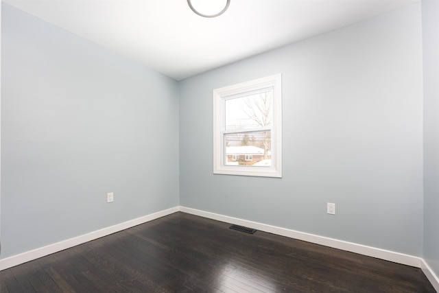 empty room featuring dark wood-type flooring, visible vents, and baseboards