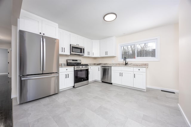 kitchen featuring light stone counters, stainless steel appliances, a sink, visible vents, and white cabinetry